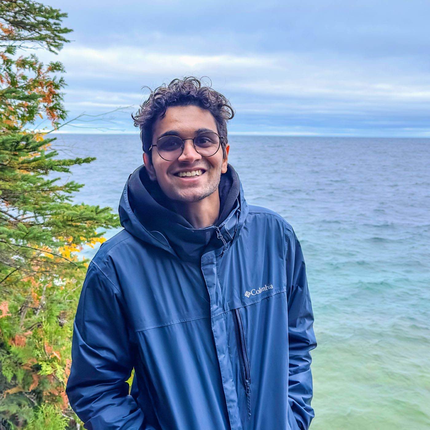 Anam Sanghavi standing by the shore of a Great Lake on a clear autumn day